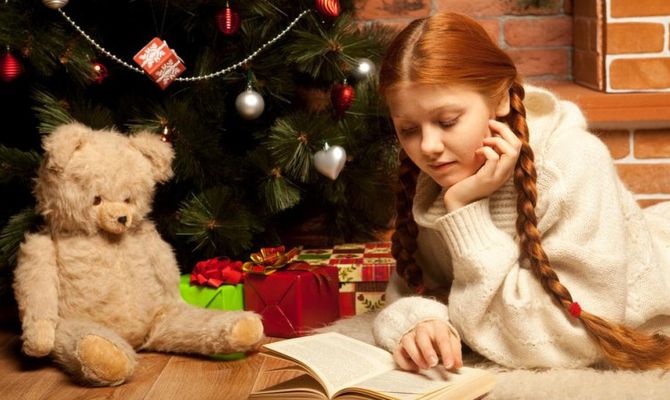Bambina legge un libro vicino all'albero di Natale